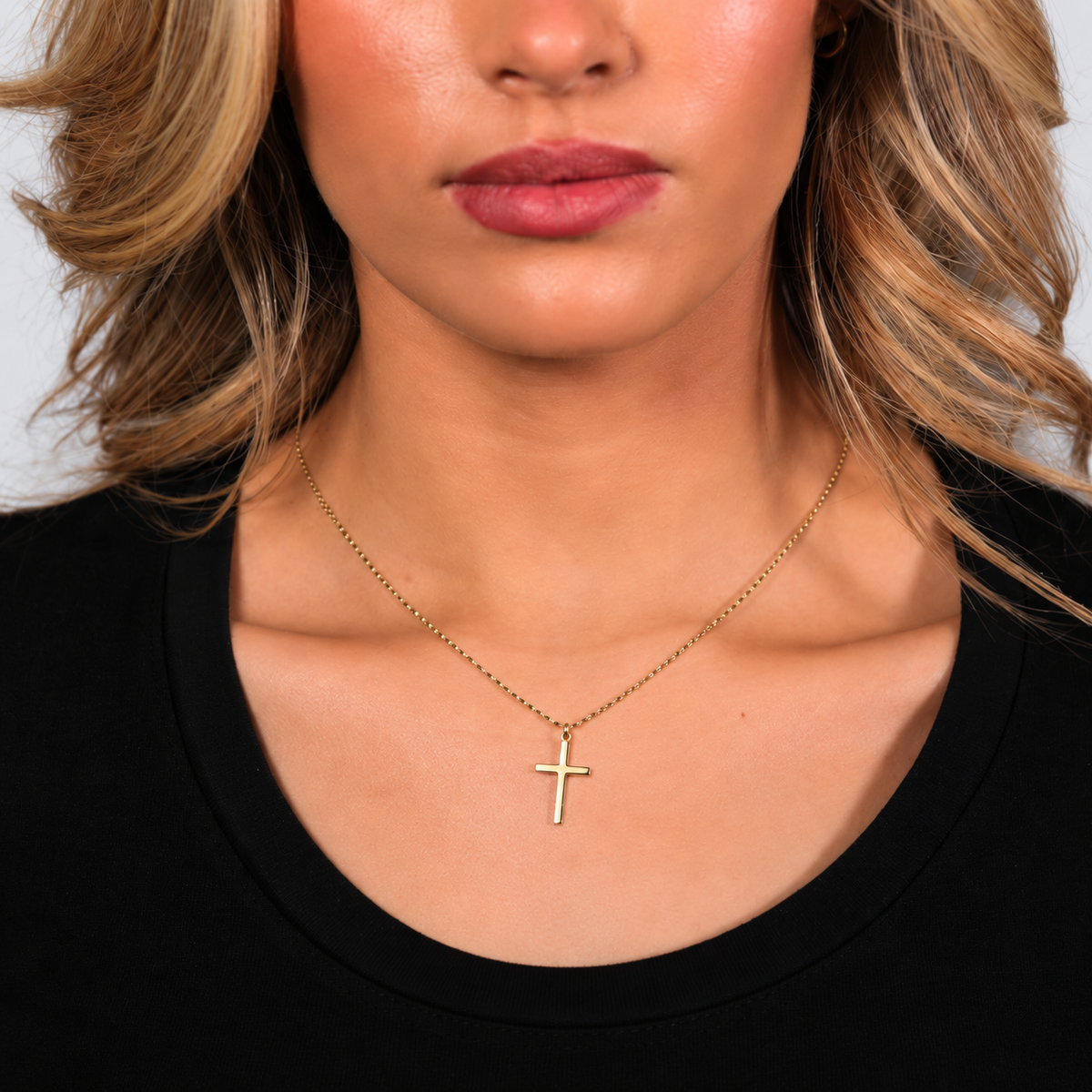 Gold cross necklace on a woman, square crop showing the lower half of her face