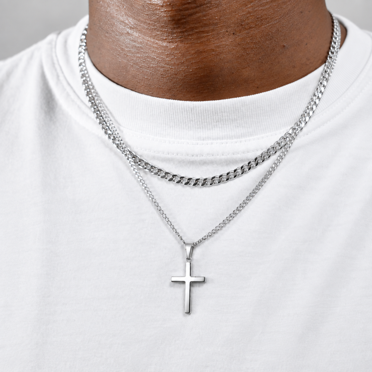 Polished silver cross pendant with layered silver chains on a white T-shirt, square lifestyle photo