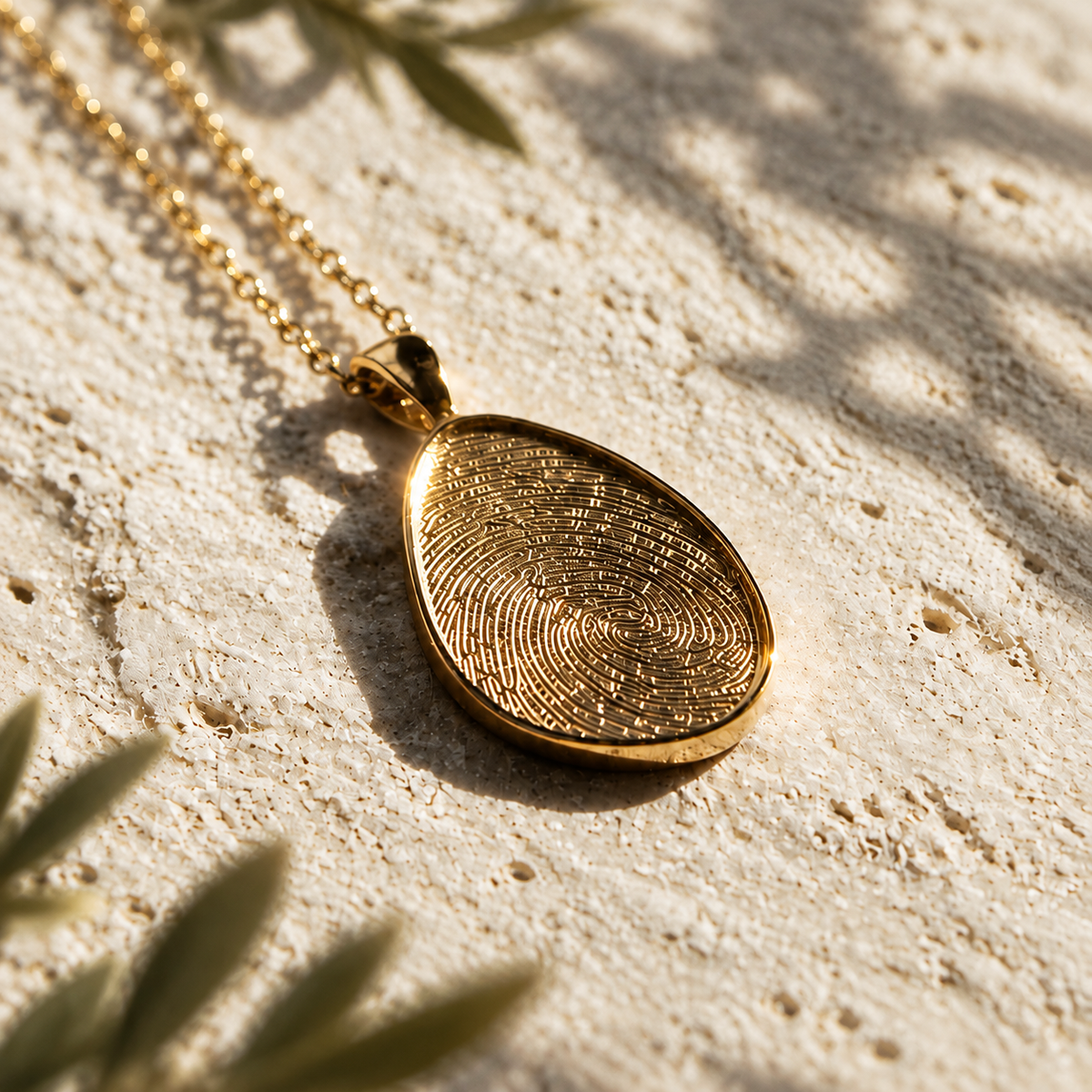 Gold fingerprint pendant and chain on cream textured stone in warm sunlight
