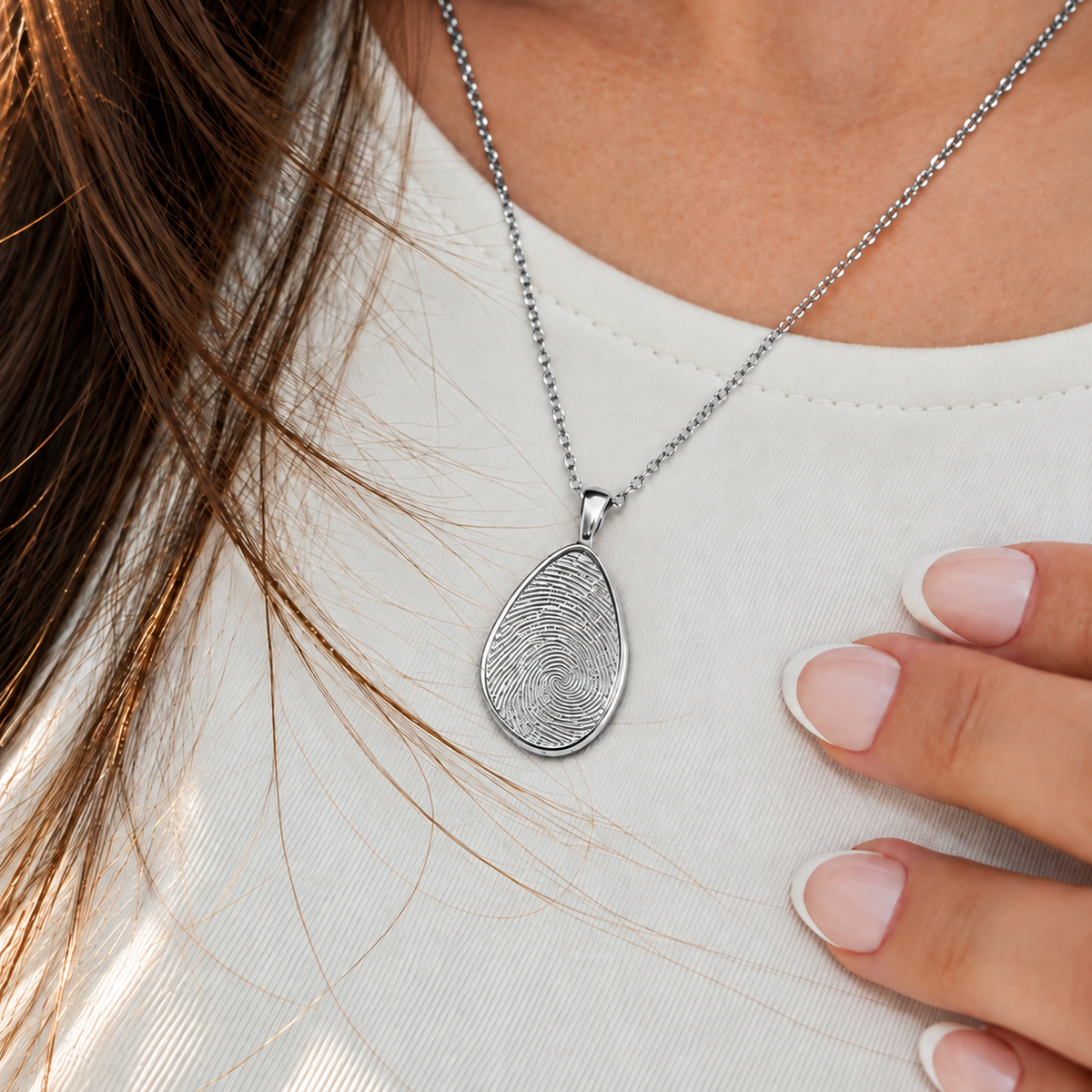 Silver fingerprint pendant worn over a white top beside French manicure nails