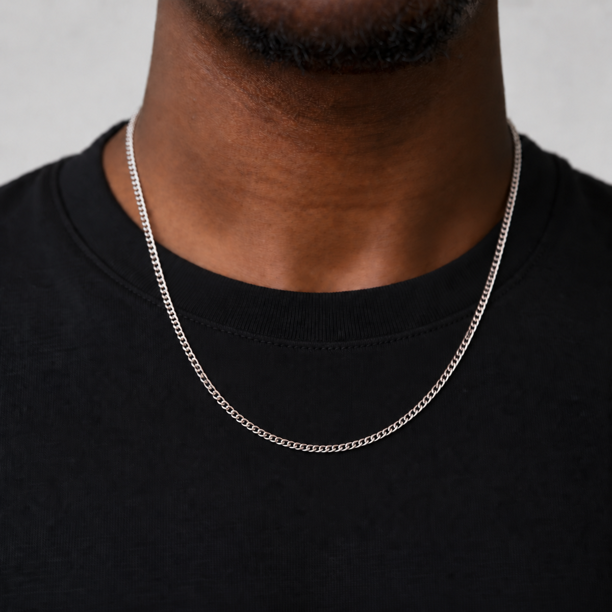 2mm silver Cuban chain, corrected 55cm upper-chest drop, black tee model photograph on Unveiled grey.