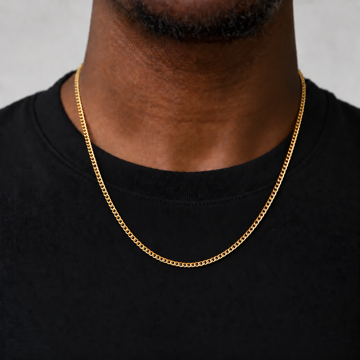 2mm 18k PVD gold Cuban chain, corrected 55cm upper-chest drop, black tee model photograph on Unveiled grey.