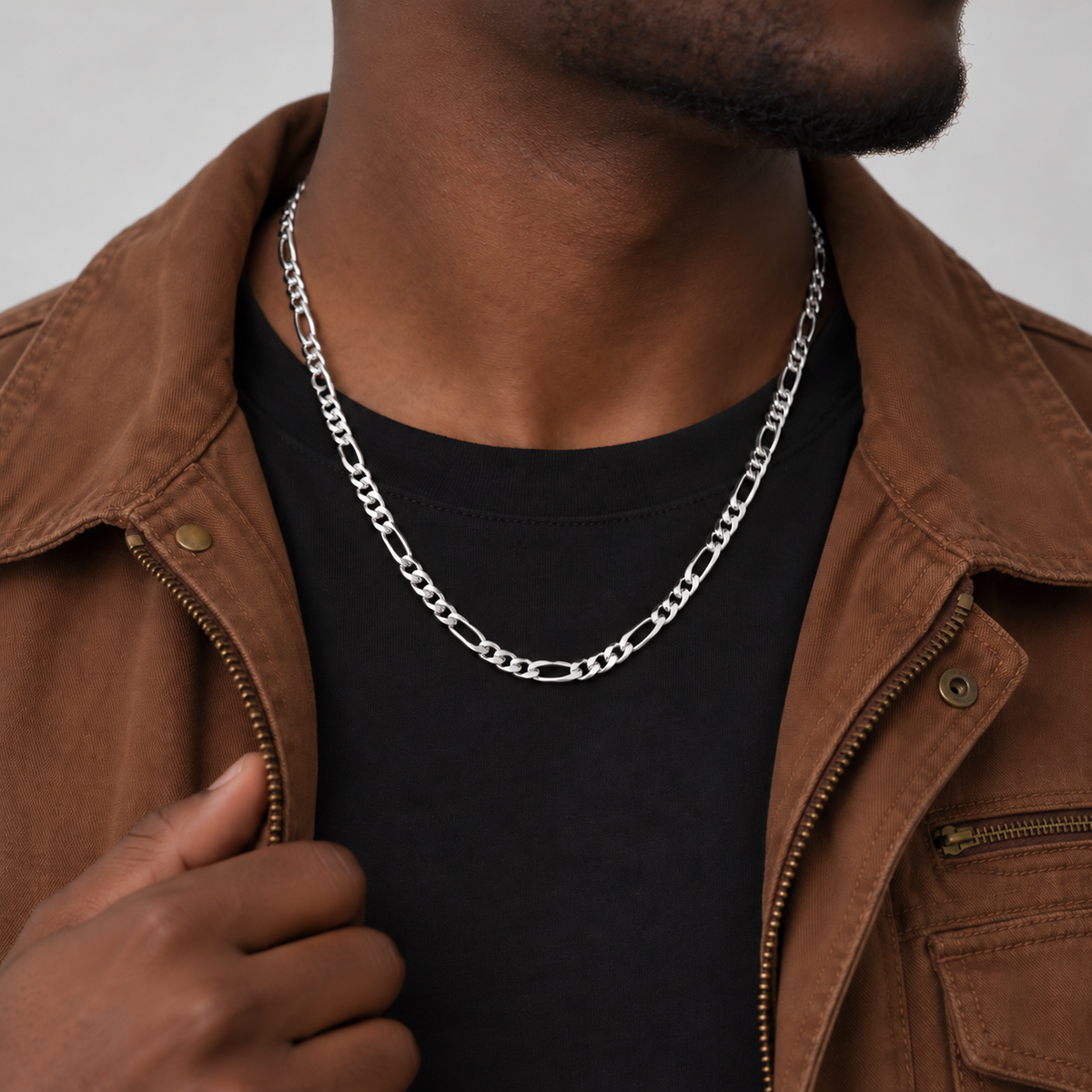 Unveiled 5mm Figaro chain in stainless steel silver, 50cm, worn by the Unveiled model in a brown canvas jacket