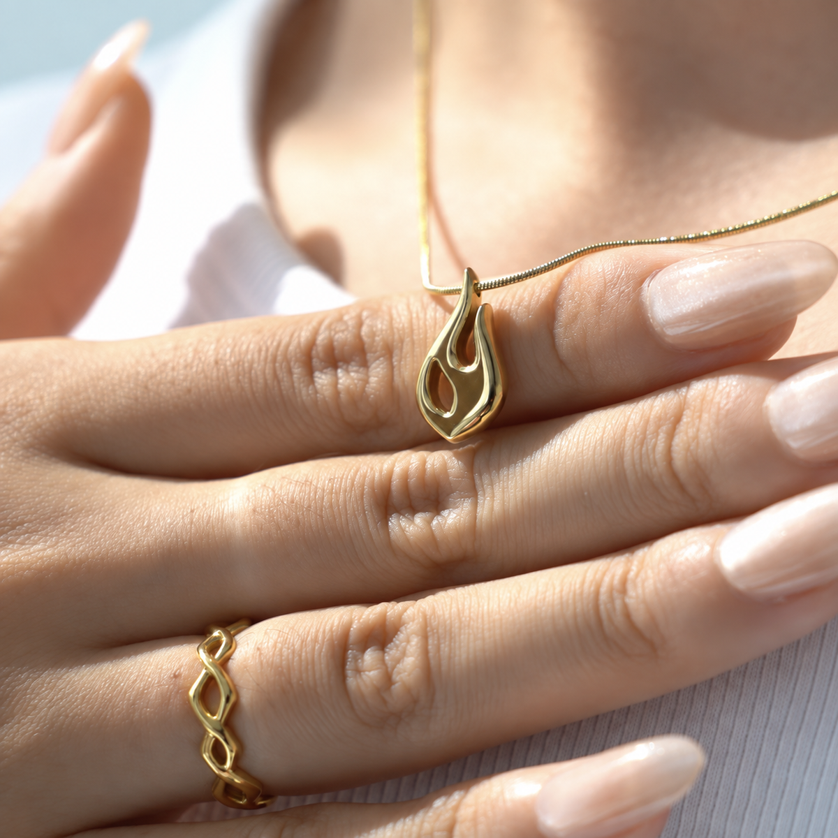 Flame pendant in gold resting against a hand with a matching dainty ring