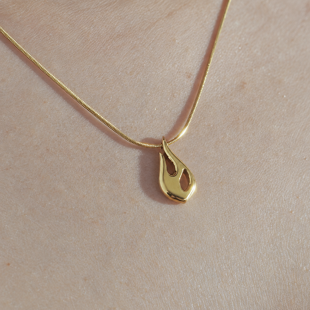 Close-up of the gold Flame pendant and snake chain worn on skin