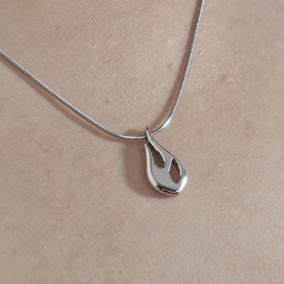 Close-up of the silver Flame pendant and snake chain worn on skin