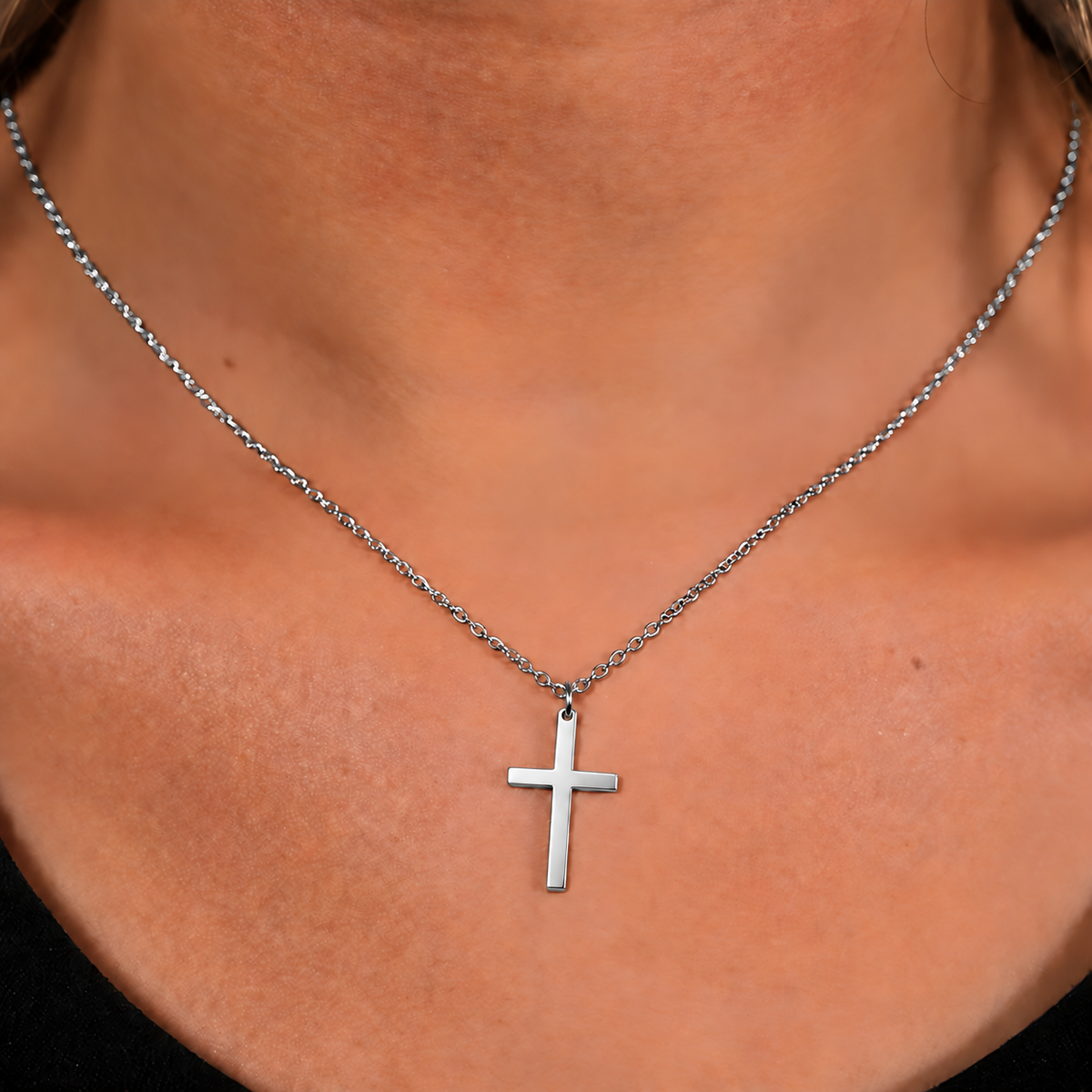 Close-up of a polished stainless-steel silver cross and chain worn by a woman