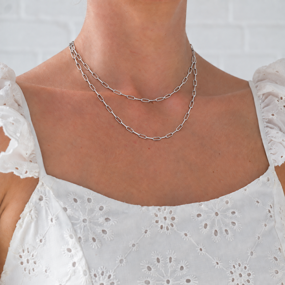 Two silver paperclip necklaces layered on a model wearing a white embroidered dress