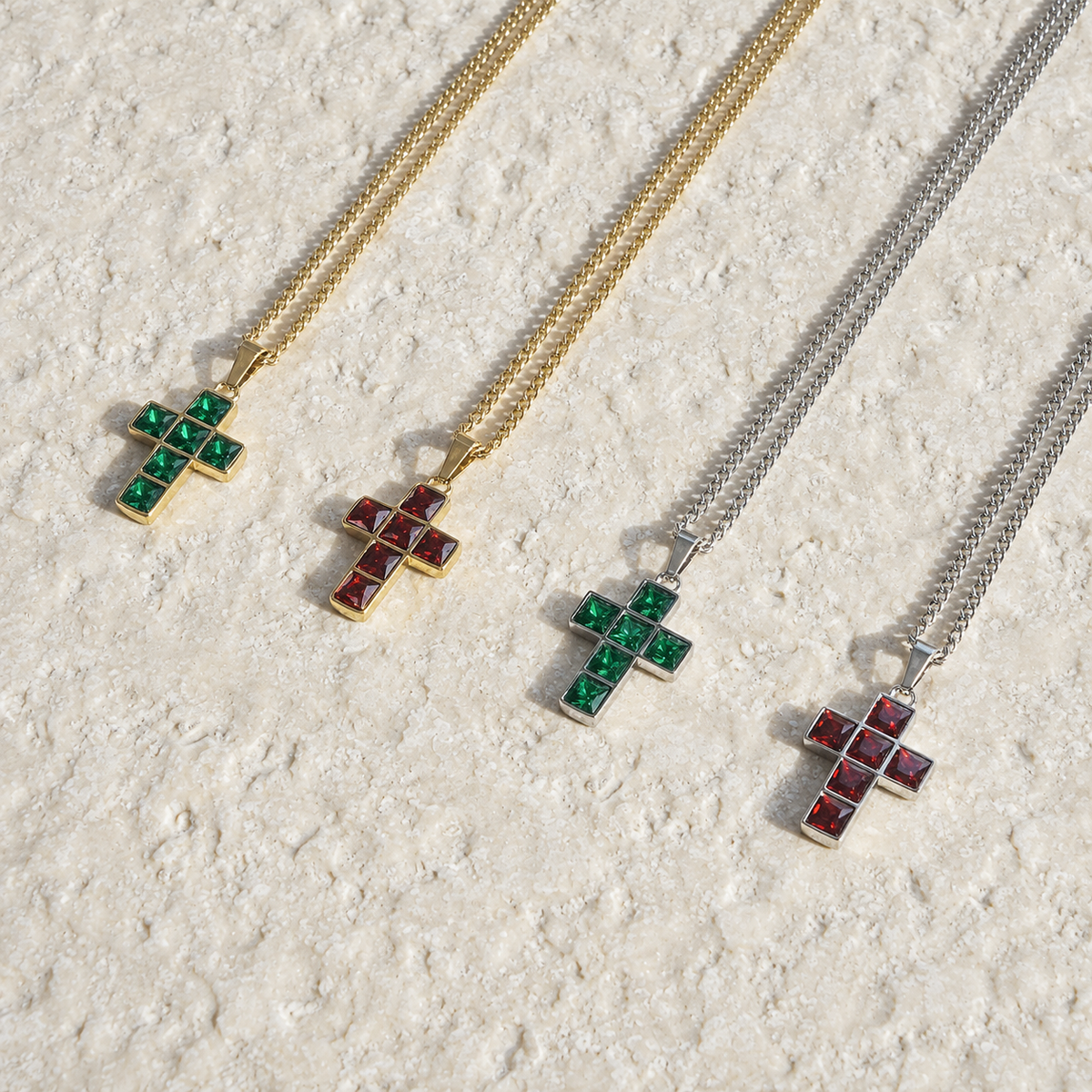 Gold and silver Purity Cross necklaces with green and red stones on cream stone