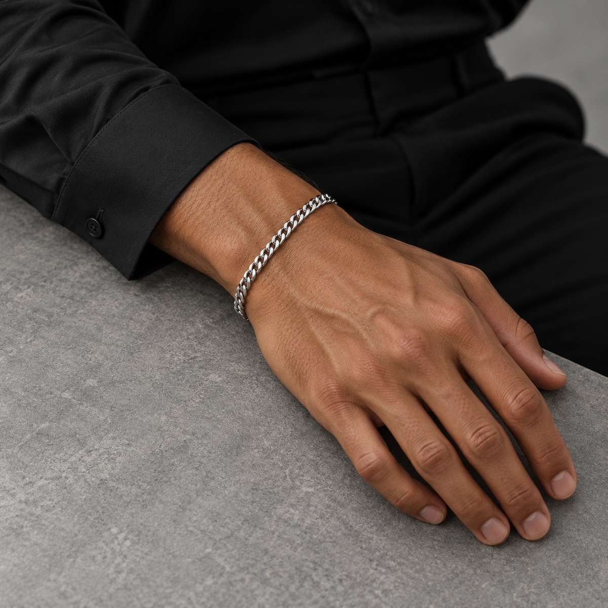 Silver 4mm Cuban bracelet on tanned model in black silk shirt, tabletop view