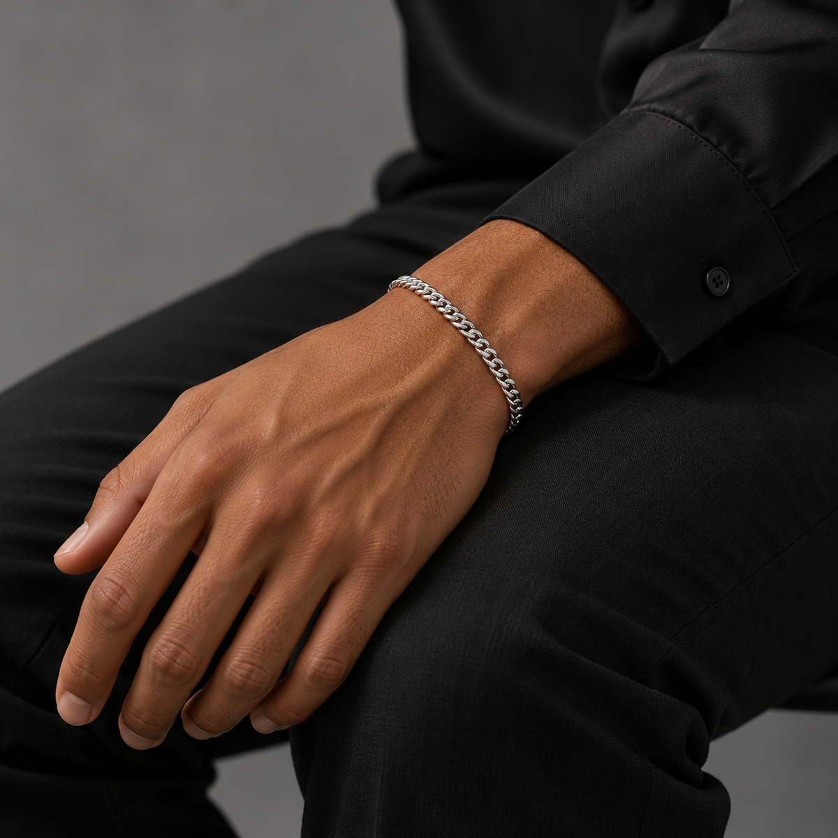 Silver 4mm Cuban bracelet on tanned model in black silk shirt, seated view