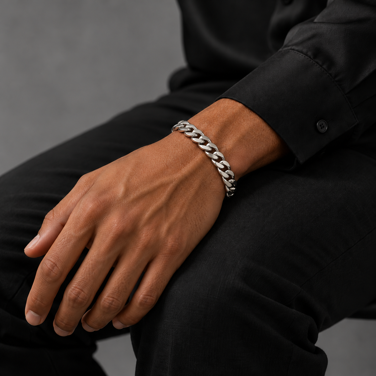 Silver 8mm Cuban bracelet on tanned model in black silk shirt, seated view