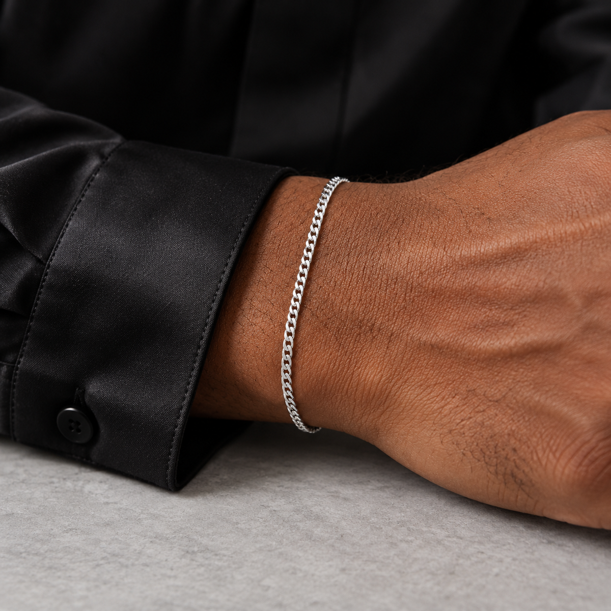 Silver 2mm Cuban bracelet beside a black silk cuff, close-up
