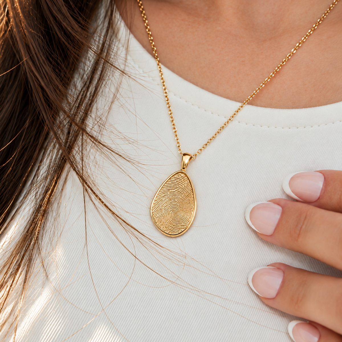 Gold fingerprint pendant necklace worn over a white top, showing fine fingerprint engraving